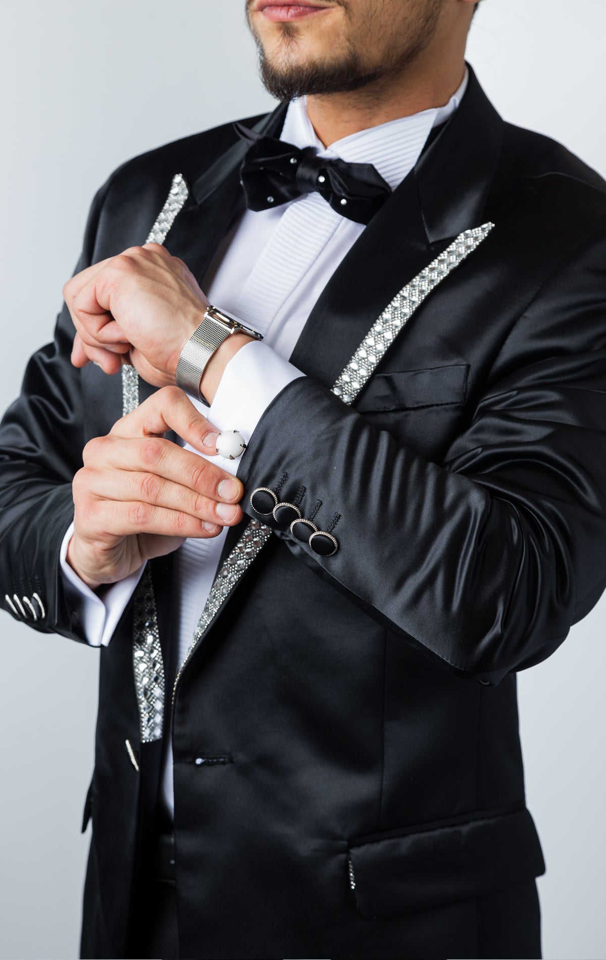 Black, one-button tuxedo jacket with a slim fit. The jacket features a shiny black fabric, rhinestone embellishments on the collar, a pocket square, and button cuffs. The jacket is made from a medium-lightweight fabric.